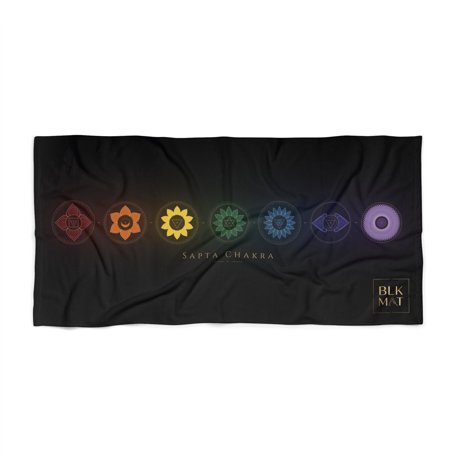 Black beach towel with a row of seven rainbow-colored chakra emblems above the caption Sapta Chakra and a small gold BLKMAT logo in the bottom-right corner.